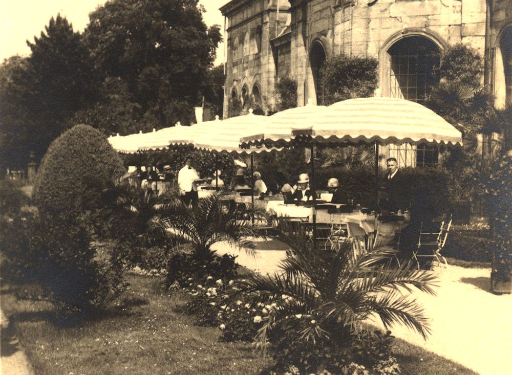 Schon drei Jahrzehnte vor dem „Orangerie-Café“ gab es in der Orangerie Kaffee: Der Besitzer des renommierten „Café Leidel“ richtete im „Lorbeerhaus“ ein Café ein und stellte in den Sommermonaten für die Besucher Tische, Stühle und Sonnenschirme vor das Gebäude (links). Ein interessantes Detail: Der damals noch existierende Weg direkt vor der Gebäudefront ist seit Jahrzehnten mit Gras zugewachsen und heute nicht mehr sichtbar. (Foto: MRV)
