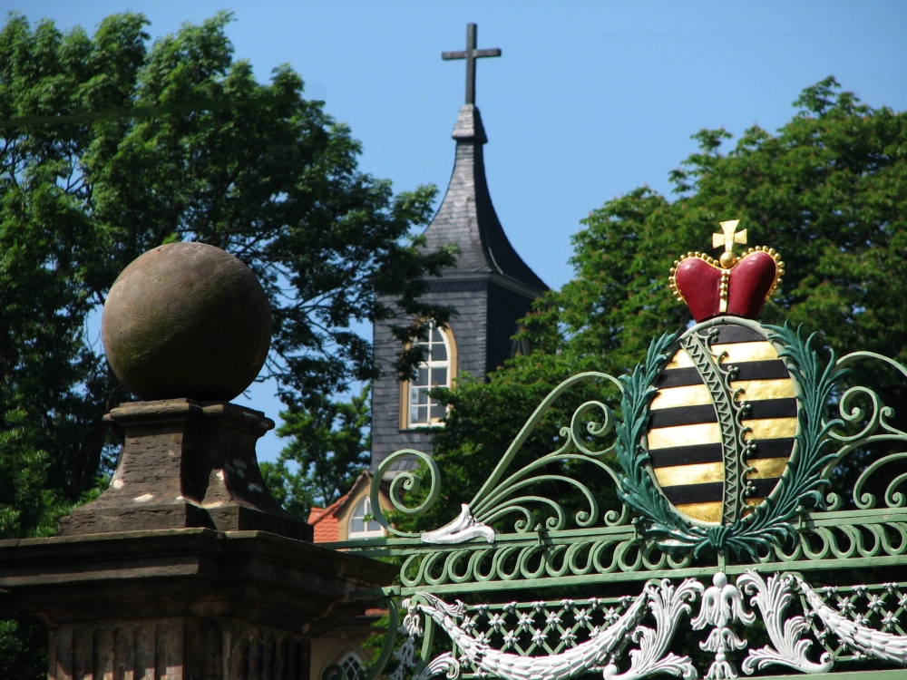 Detailansicht des Portals mit sächsischem Rautenkranzwappen und Pfeilerbekrönung vor dem Hintergrund des Turmes des neogotischen „Teeschlösschens“, das sich südwestlich oberhalb der Gartenanlage erhebt. (Foto: Cramer)